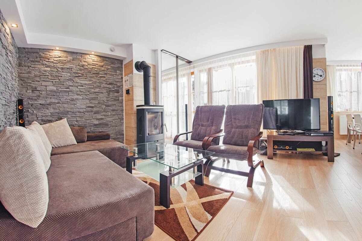 Ein modernes Wohnzimmer mit Steinwand, Kamin, Glastisch und Flachbildfernseher.