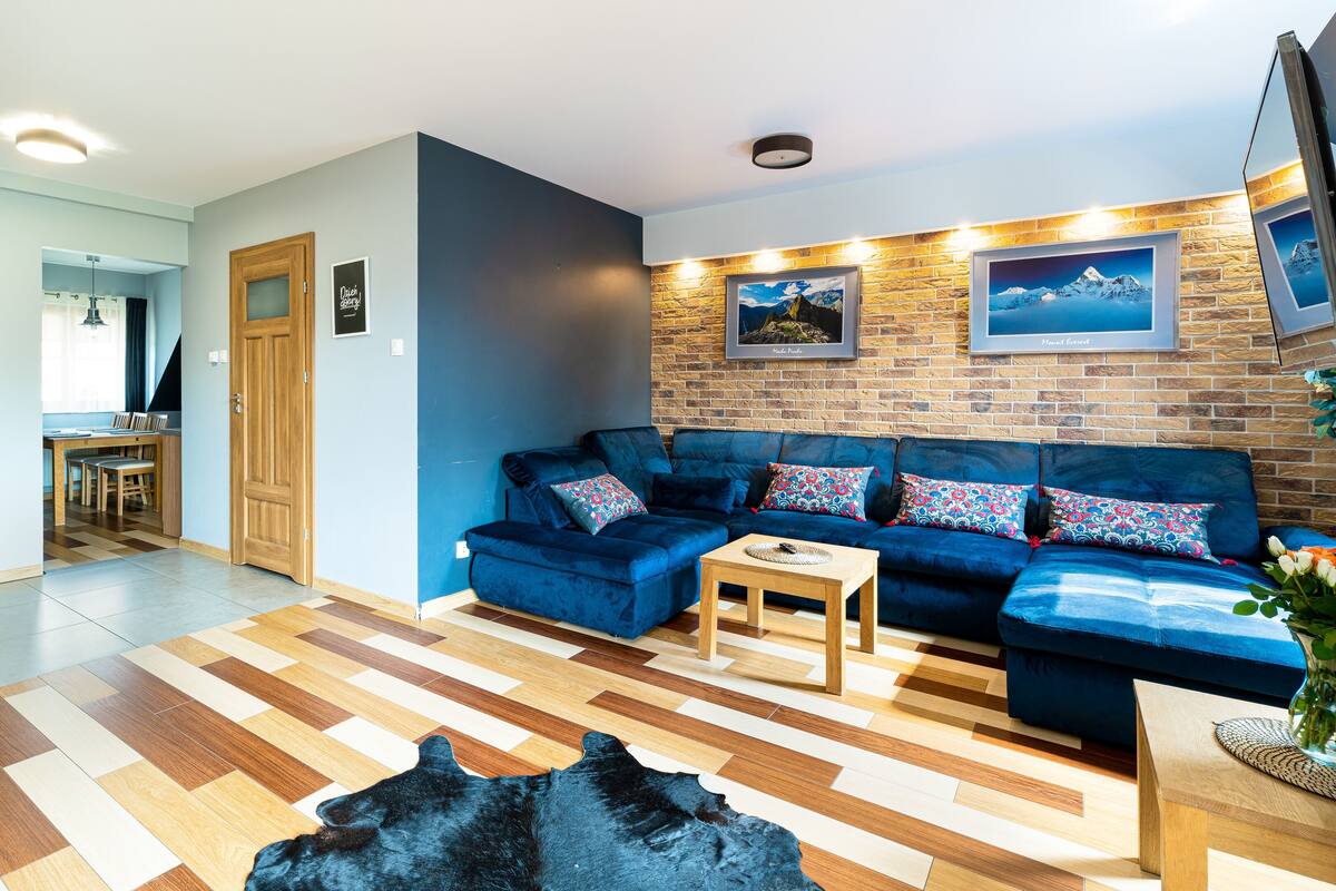 Ein modernes Wohnzimmer mit einem blauen Sofa, einem Holztisch und einem gemusterten Teppich.
