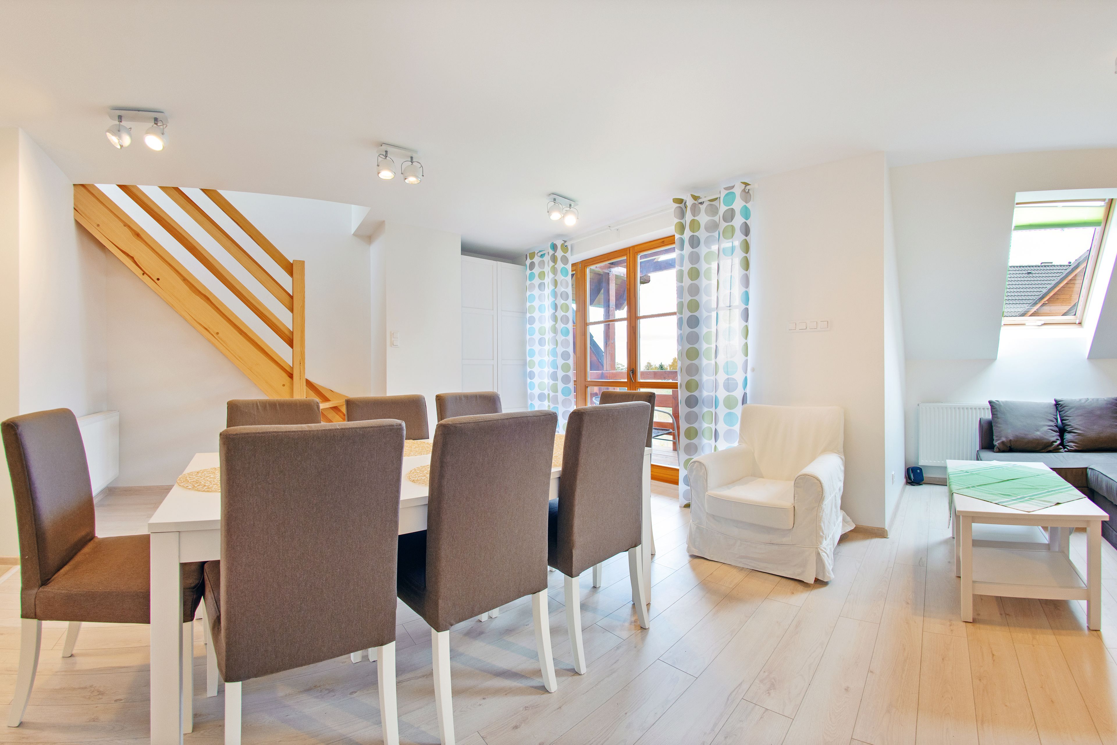 A dining area with a wooden staircase, white walls, and a view of the outside.