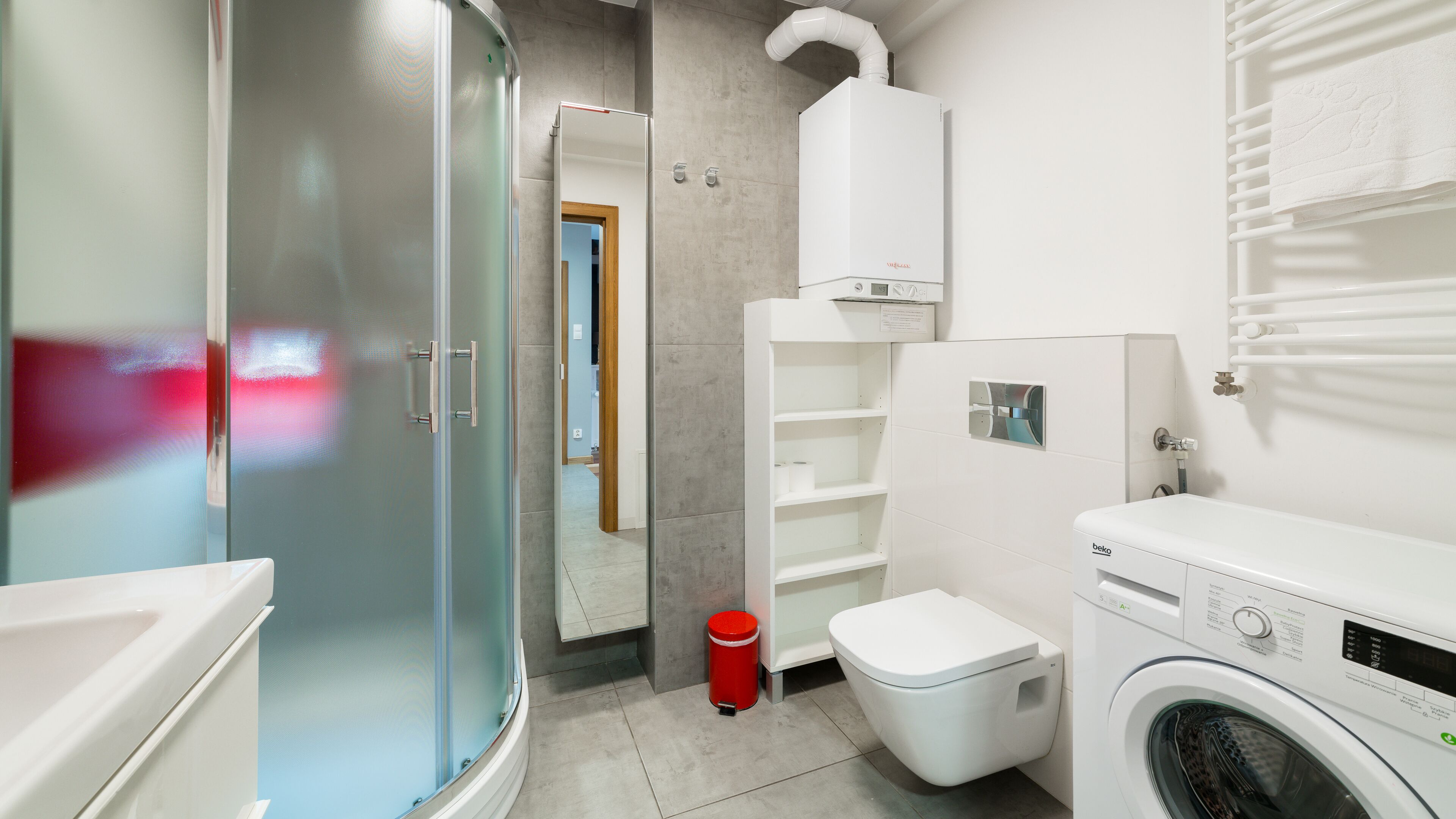 Un baño moderno con cabina de ducha de vidrio, inodoro, lavadora y barra para toallas.