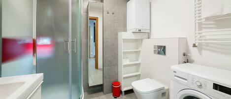 Un baño moderno con cabina de ducha de vidrio, inodoro, lavadora y barra para toallas.