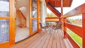 A wooden deck with a table and chairs, a wooden staircase, and large glass doors leading to an interior space. - Apartamenty Sun & Snow Komuny Paryskiej (Karpacz)