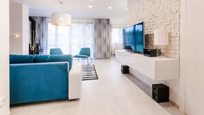 A modern living room with a blue sofa, a white entertainment unit, and a large TV. - Apartamenty Sun & Snow Komuny Paryskiej (Karpacz)
