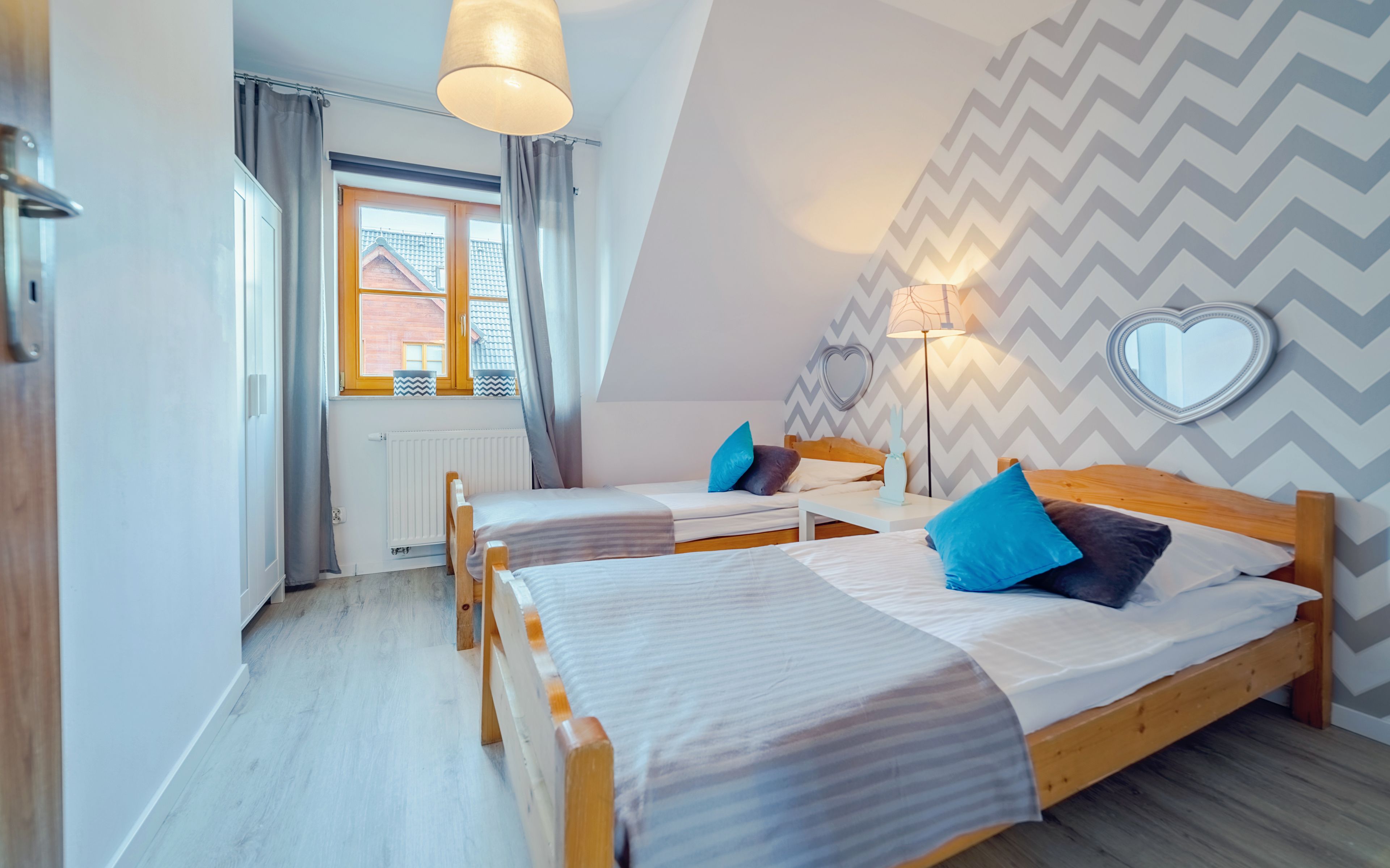 A bedroom with two wooden beds, a window with curtains, a radiator, and a chevron-patterned wall.