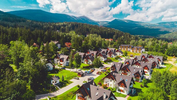 A residential area with houses featuring sloped roofs and balconies, surrounded by lush greenery and mountains in the background. - Apartamenty Sun & Snow Komuny Paryskiej (Karpacz)