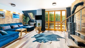 A modern living room with a blue sofa, wooden flooring, a large rug, and a staircase leading to an outdoor area. - Apartamenty Sun & Snow Komuny Paryskiej (Karpacz)