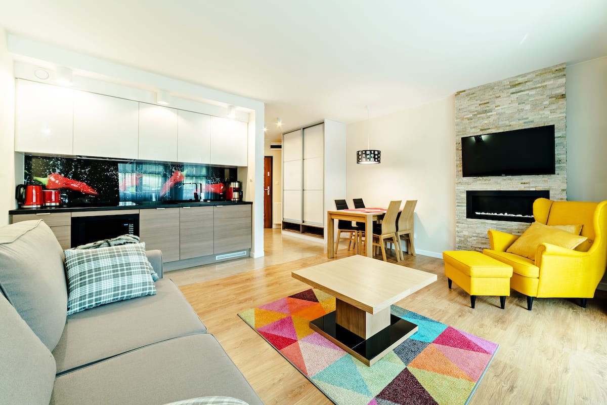 Een moderne woonkamer met een bank, een salontafel, een gele fauteuil en een aan de muur bevestigde televisie.