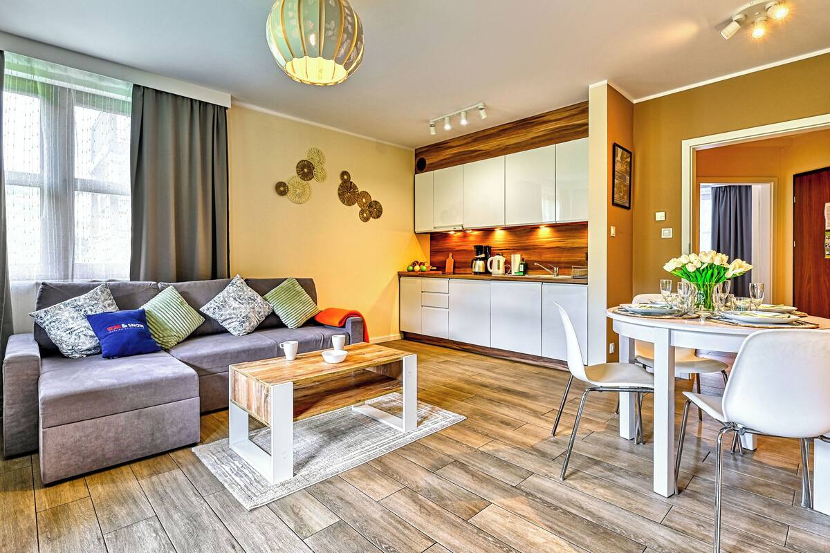 Een moderne woonkamer met een grijze bank, een salontafel en een eethoek met een witte tafel en stoelen.