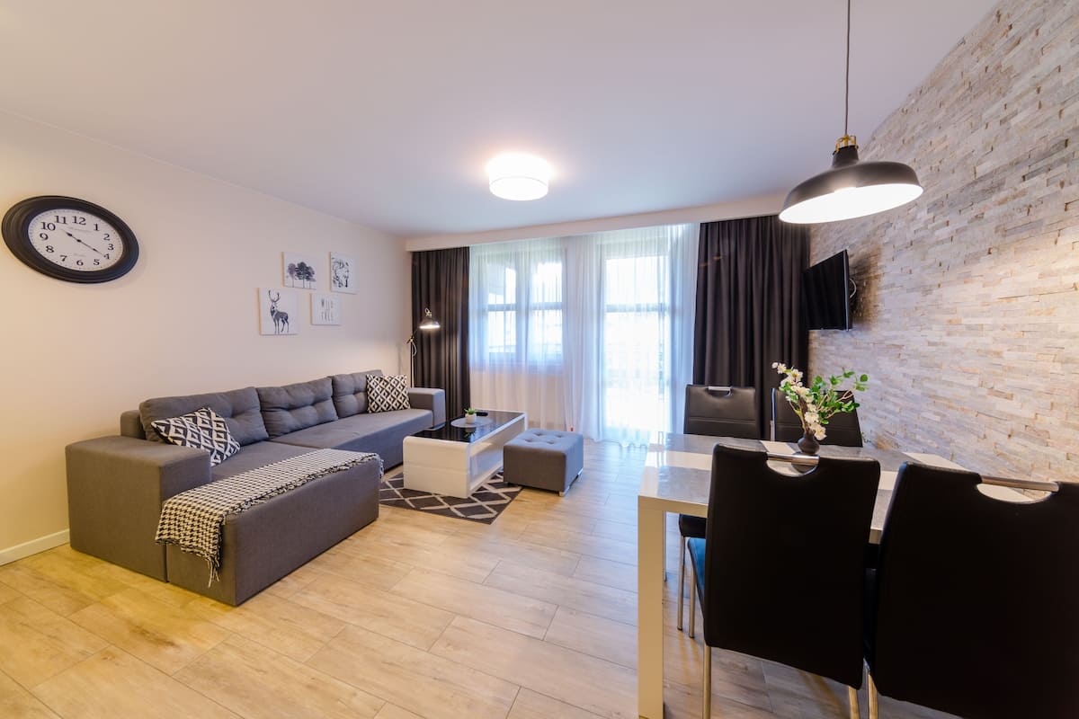 Een moderne woonkamer met een modulaire bank, een eettafel met stoelen, een salontafel en een wandklok.