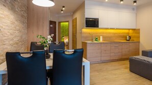 A modern kitchen with white cabinets, a microwave, and a sink. There is a dining area with a table and chairs, and a small seating area with a sofa.