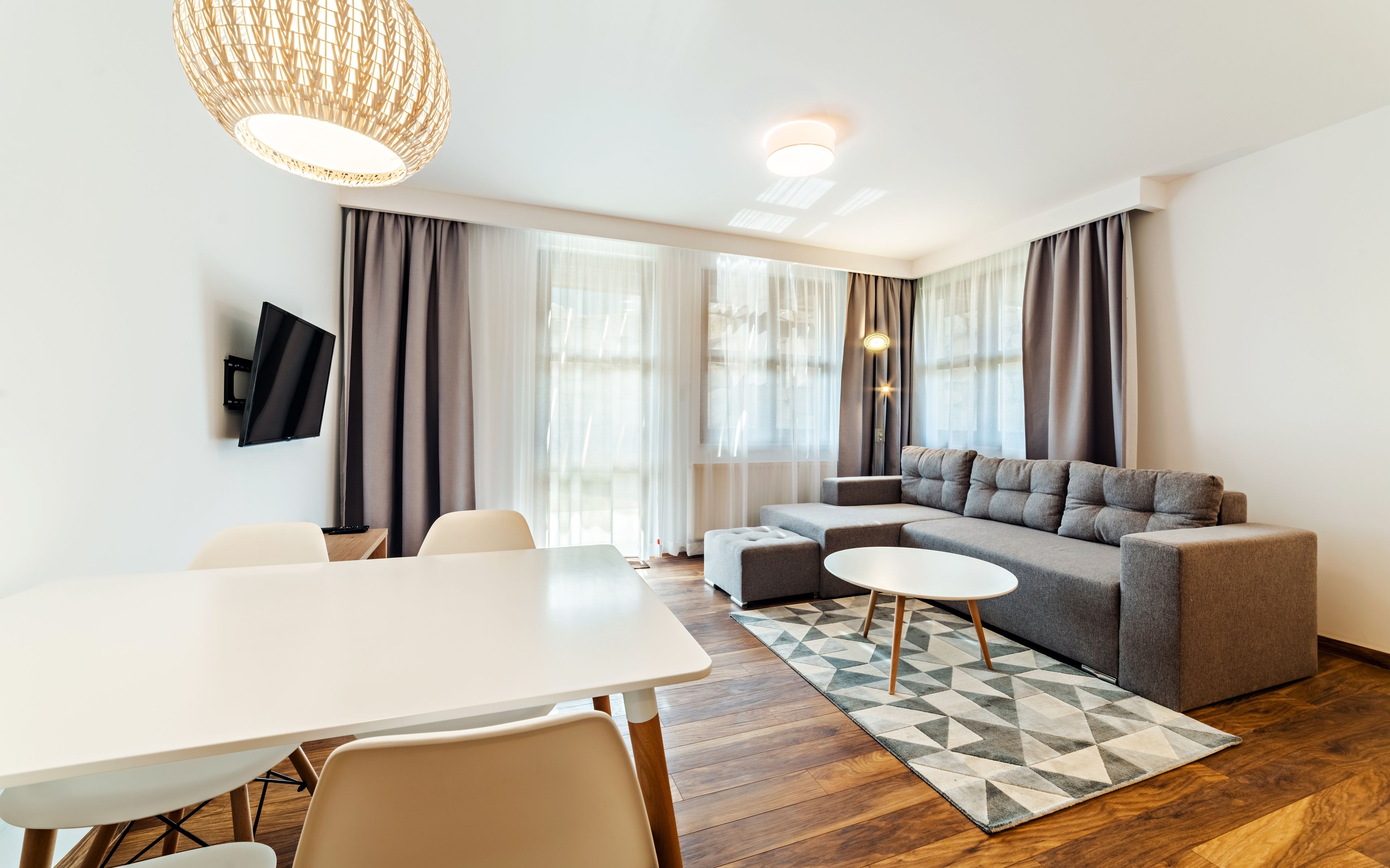 Ein modernes Wohnzimmer mit einer Couch, einem Esstisch und einem an der Wand befestigten Fernseher.