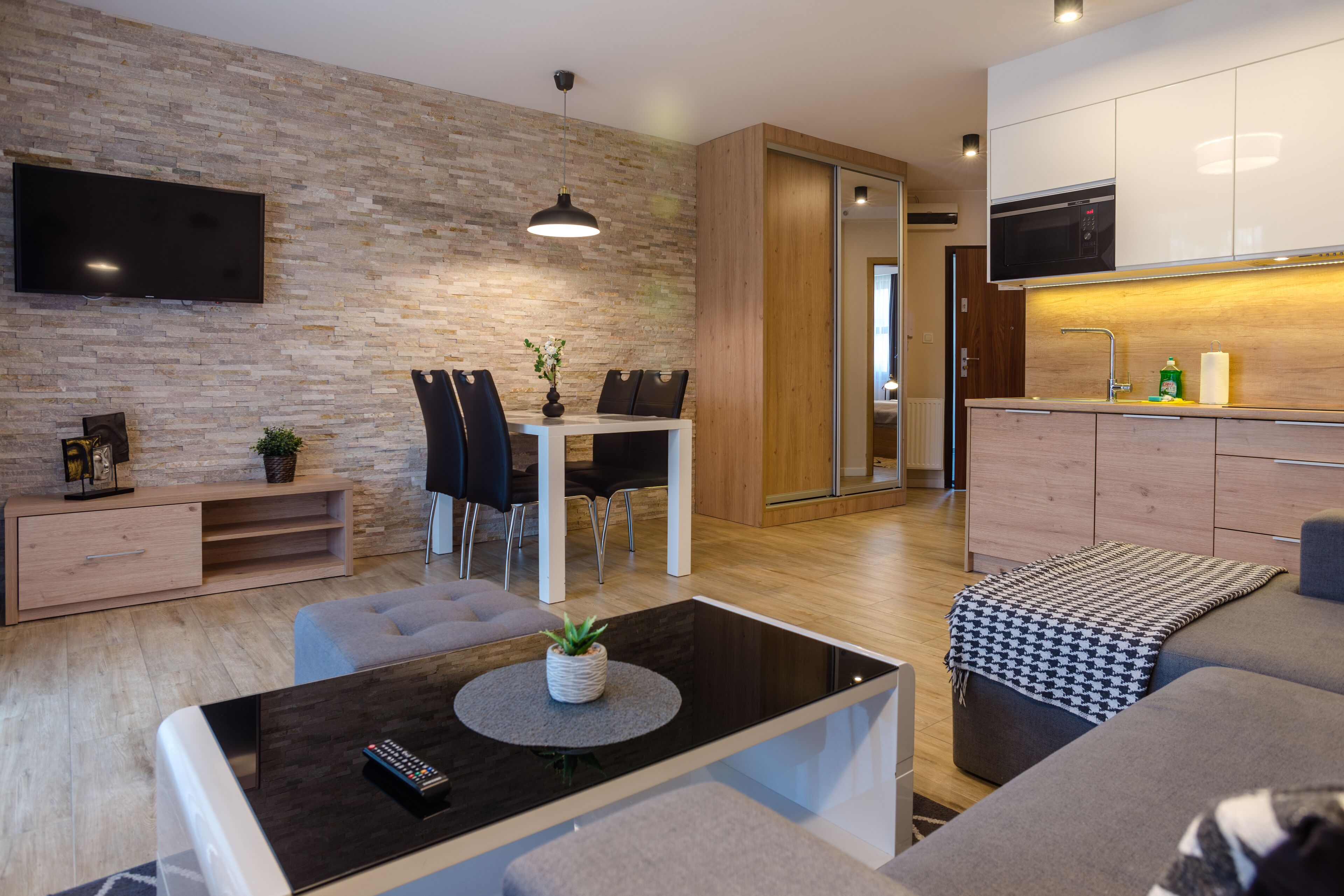 Een moderne woonkamer met een flatscreen televisie, een eethoek met tafel en stoelen, een bank en een keuken met kastjes en een magnetron.