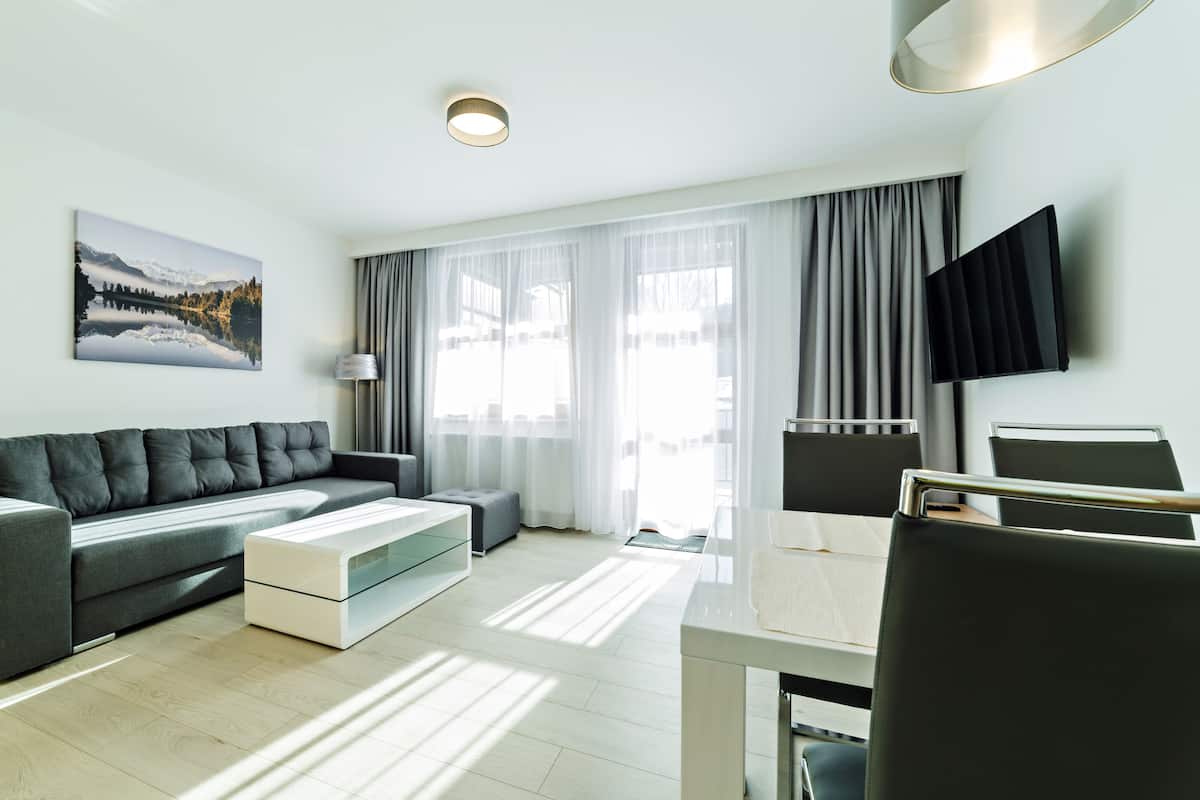 Een moderne woonkamer met een grijze bank, een witte salontafel en een aan de muur bevestigde televisie.