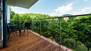 A wooden deck with two chairs and a table, overlooking a forested hillside.