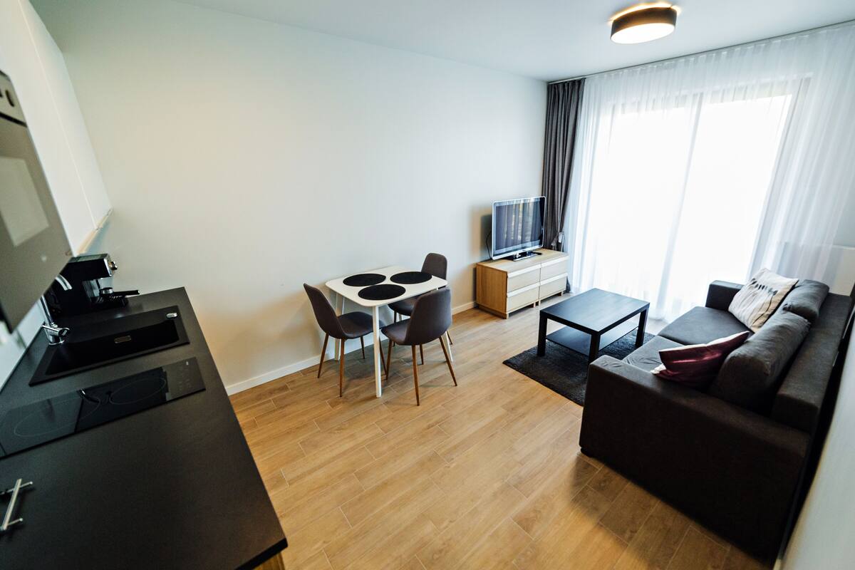 Ein modernes Wohnzimmer mit Sofa, Couchtisch, Fernseher und einem Essbereich mit Stühlen und Tisch.