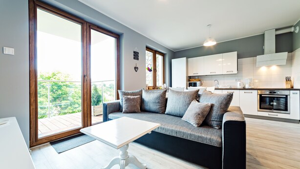 A modern living room with a sofa, a dining table, and a kitchen in the background.