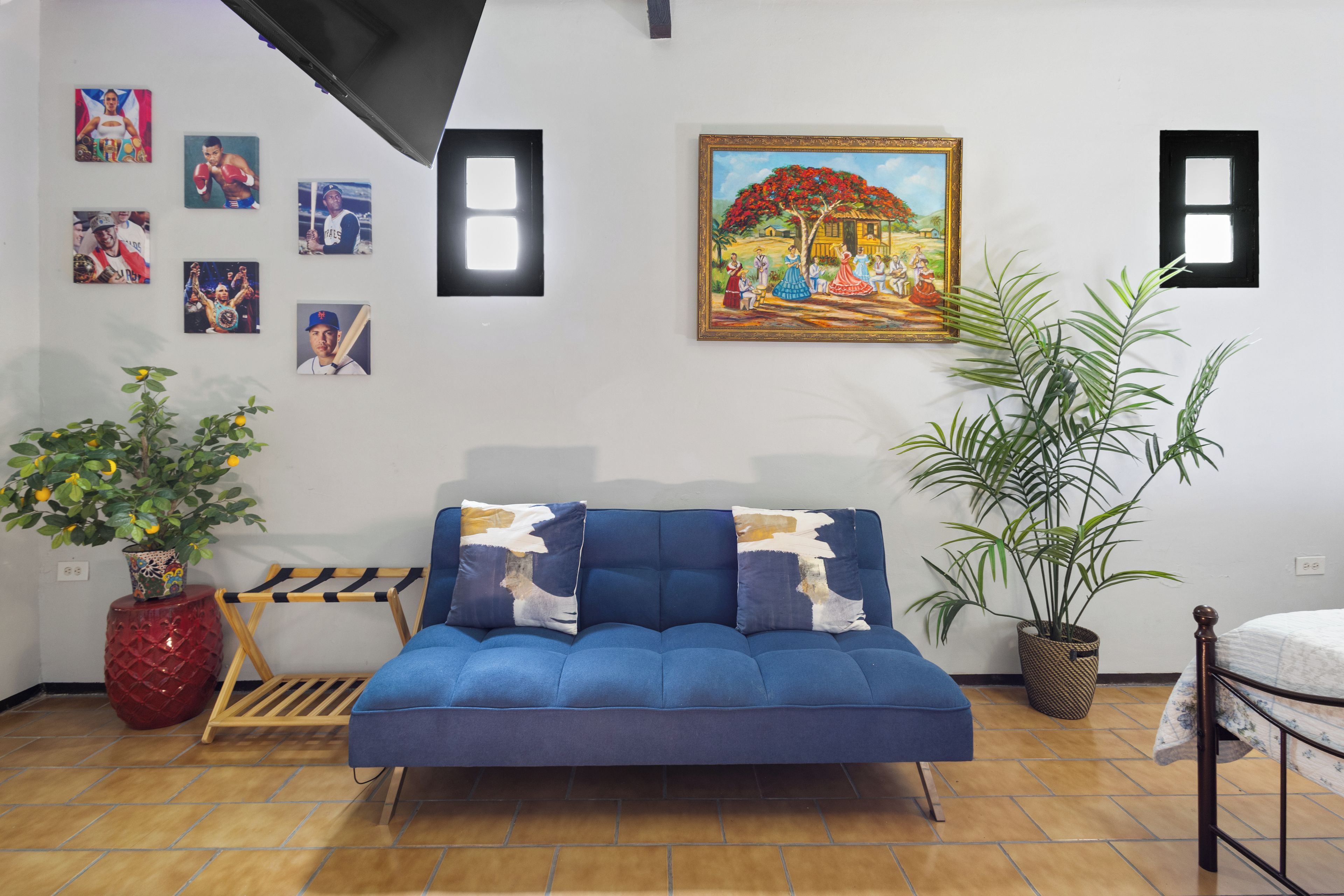 Een kamer met een blauwe bank, een schilderij en diverse ingelijste foto’s aan de muur.