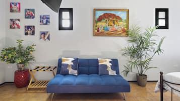 Een kamer met een blauwe bank, een schilderij en diverse ingelijste foto’s aan de muur.