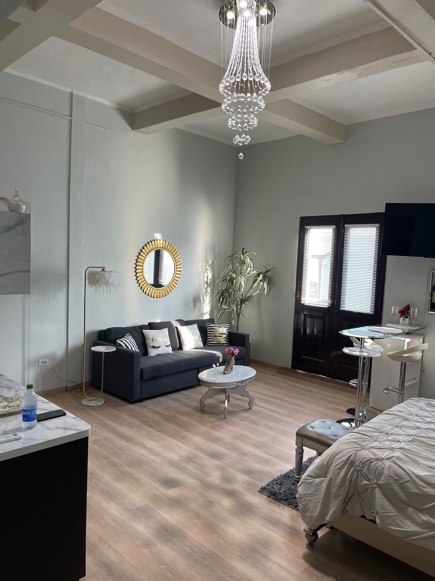 A modern bedroom with a bed, a sofa, a small round table, a mirror, and a chandelier.