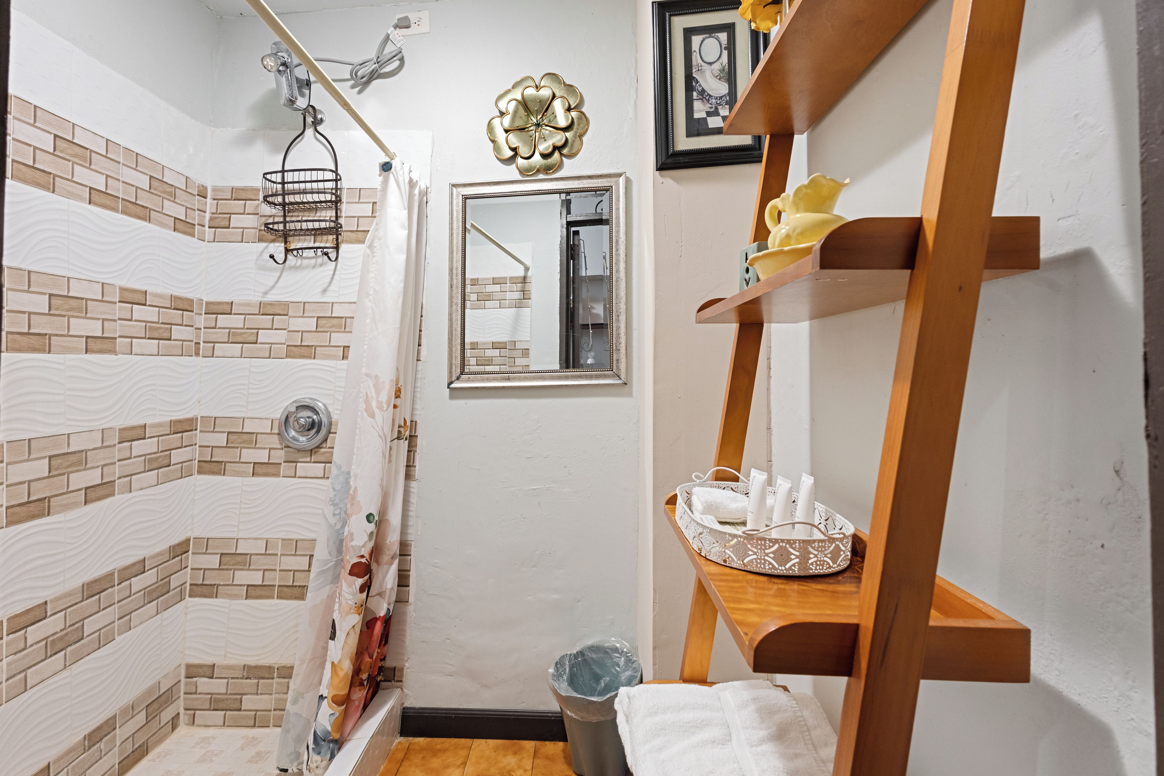 Een badkamer met een douche, een spiegel, een handdoekhouder en een plank met toiletartikelen.