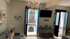 A living room with a grey sofa, a chandelier, a dining area with a table and chairs, and a TV mounted on the wall. - Casa Of Essence (San Juan)