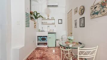Uma cozinha compacta com micro-ondas, pequena geladeira e pia. Há uma área de refeições com mesa de vidro e cadeiras.