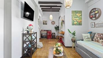 A cozy living room with a wooden coffee table, a sofa, a TV mounted on the wall, and a kitchen area in the background.