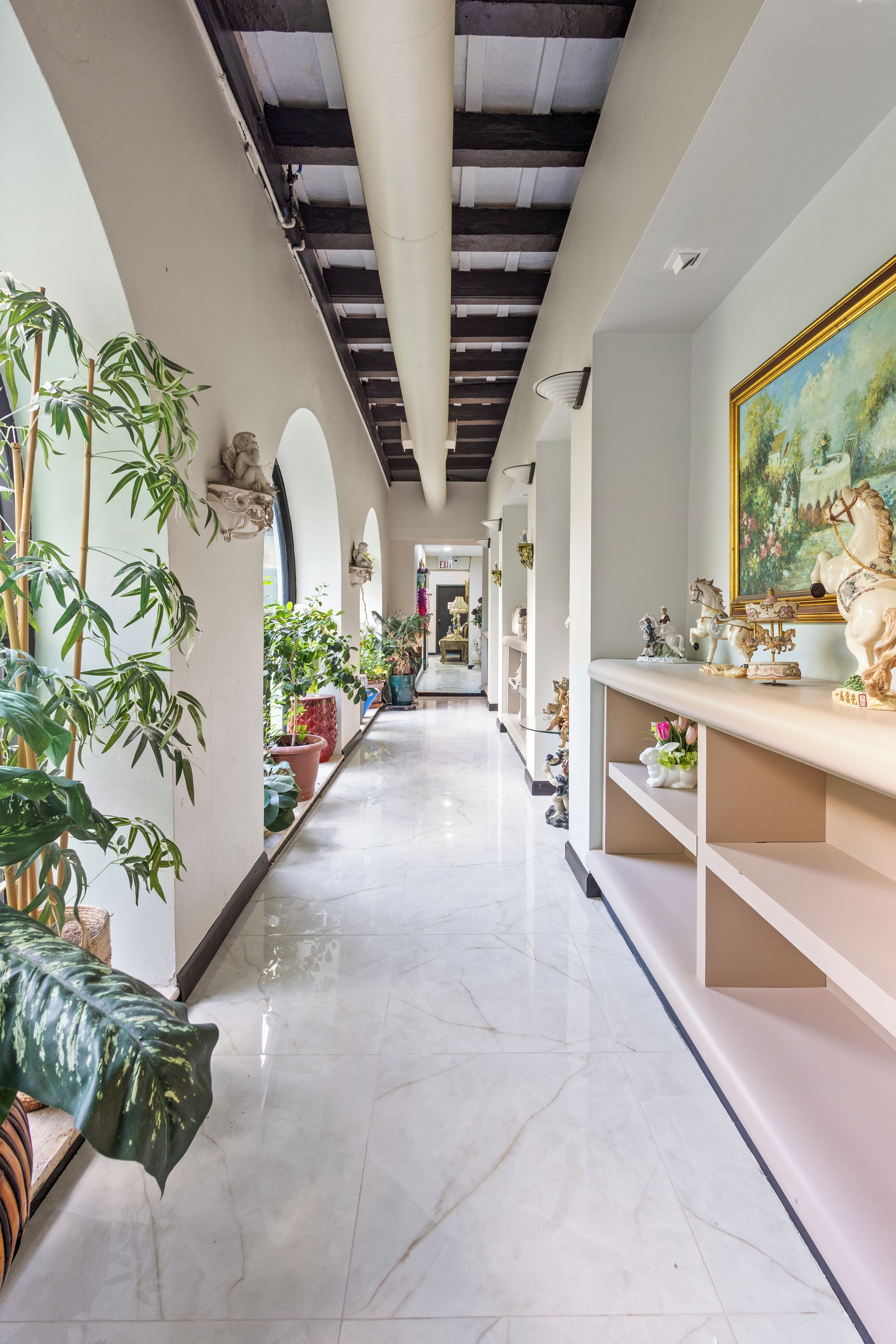 A corridor with a marble floor, potted plants, and a painting on the wall.