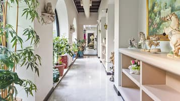 A corridor with a marble floor, potted plants, and a painting on the wall.