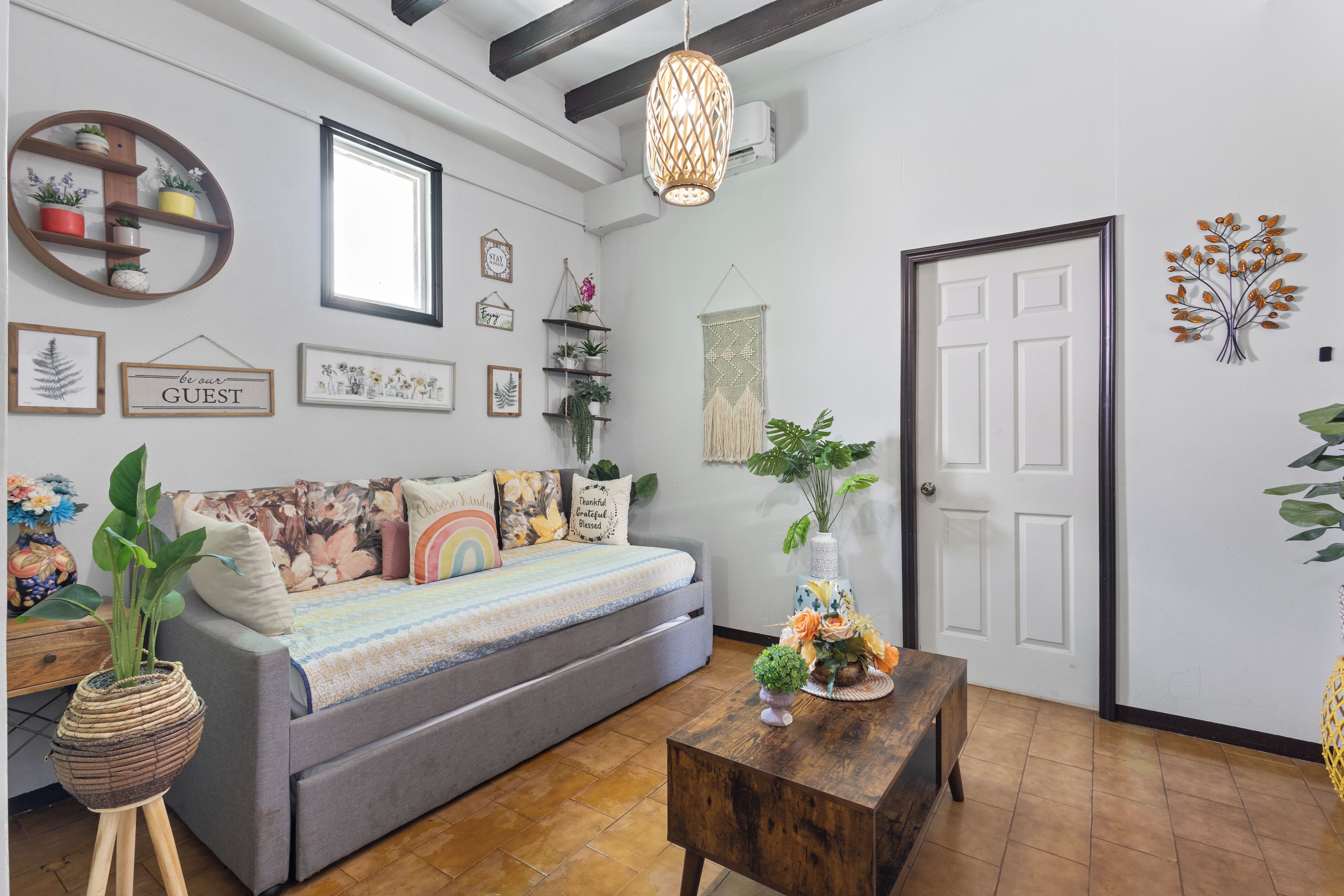 A cozy living room with a sofa, a wooden coffee table, and various wall decorations including framed pictures and a wall-mounted shelf with plants.