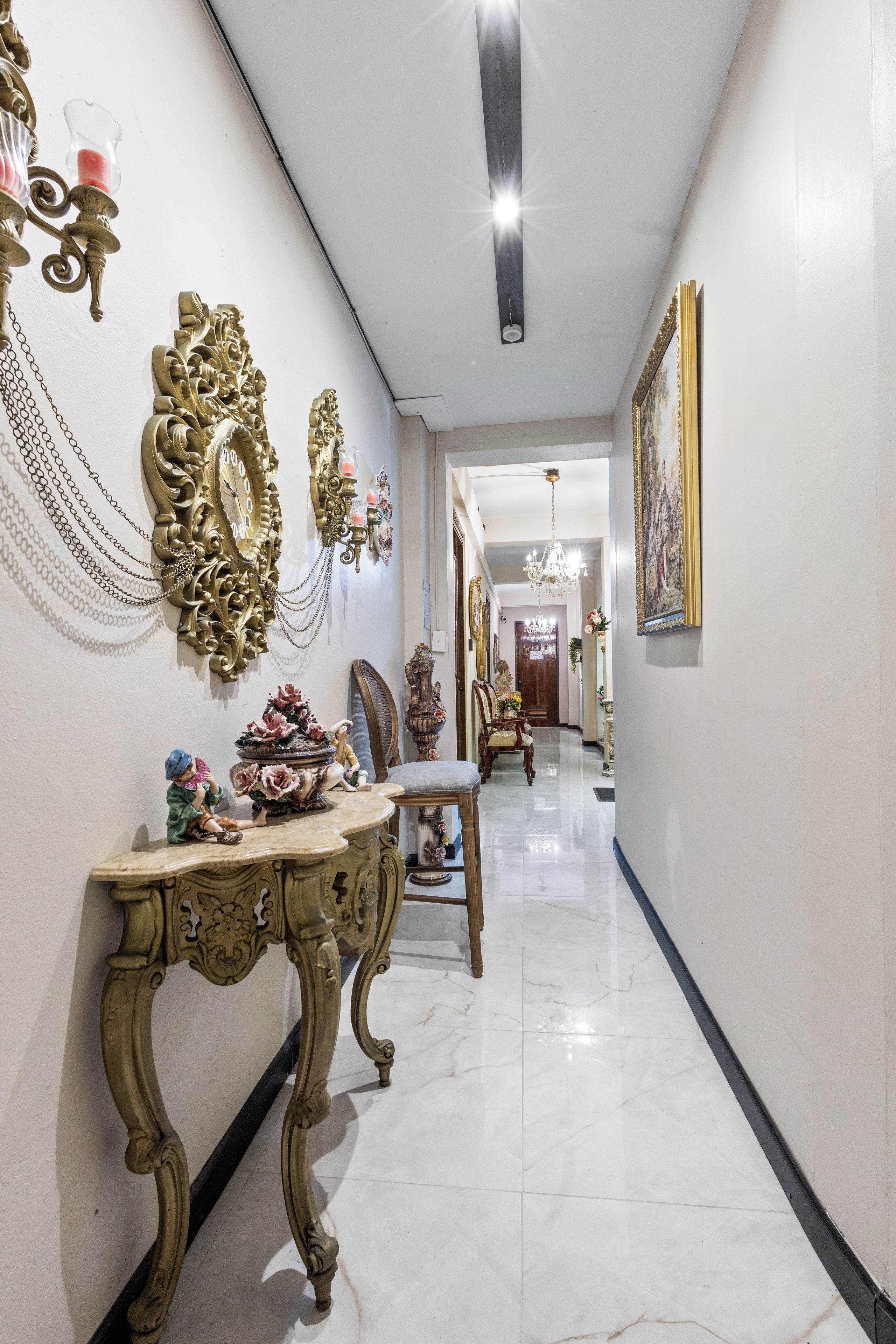 Un pasillo con decoraciones ornamentales en las paredes, suelo de mármol y un candelabro.