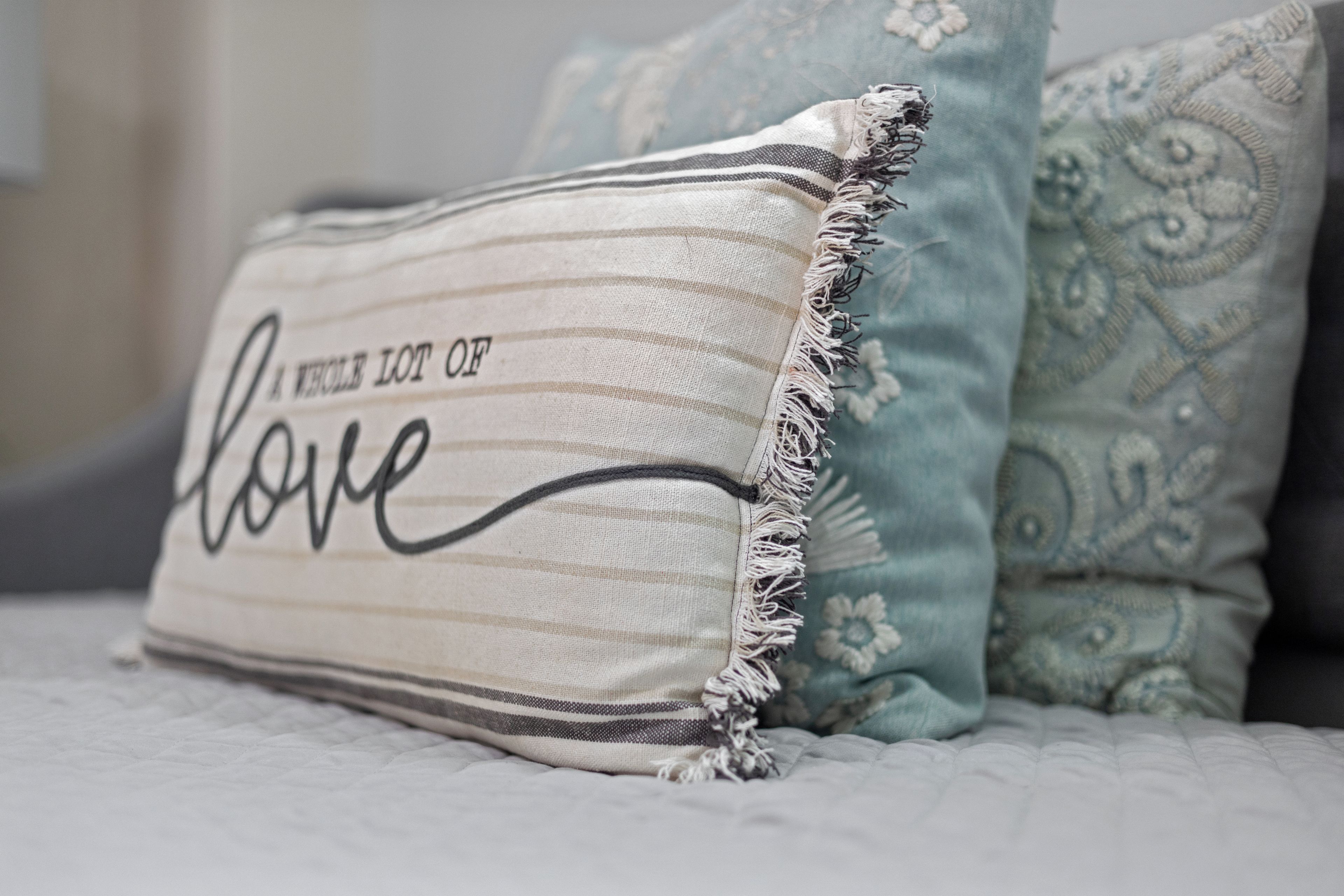 A pillow with a decorative border and a fabric with the text 'A WHOLE LOT OF love' on a bed.