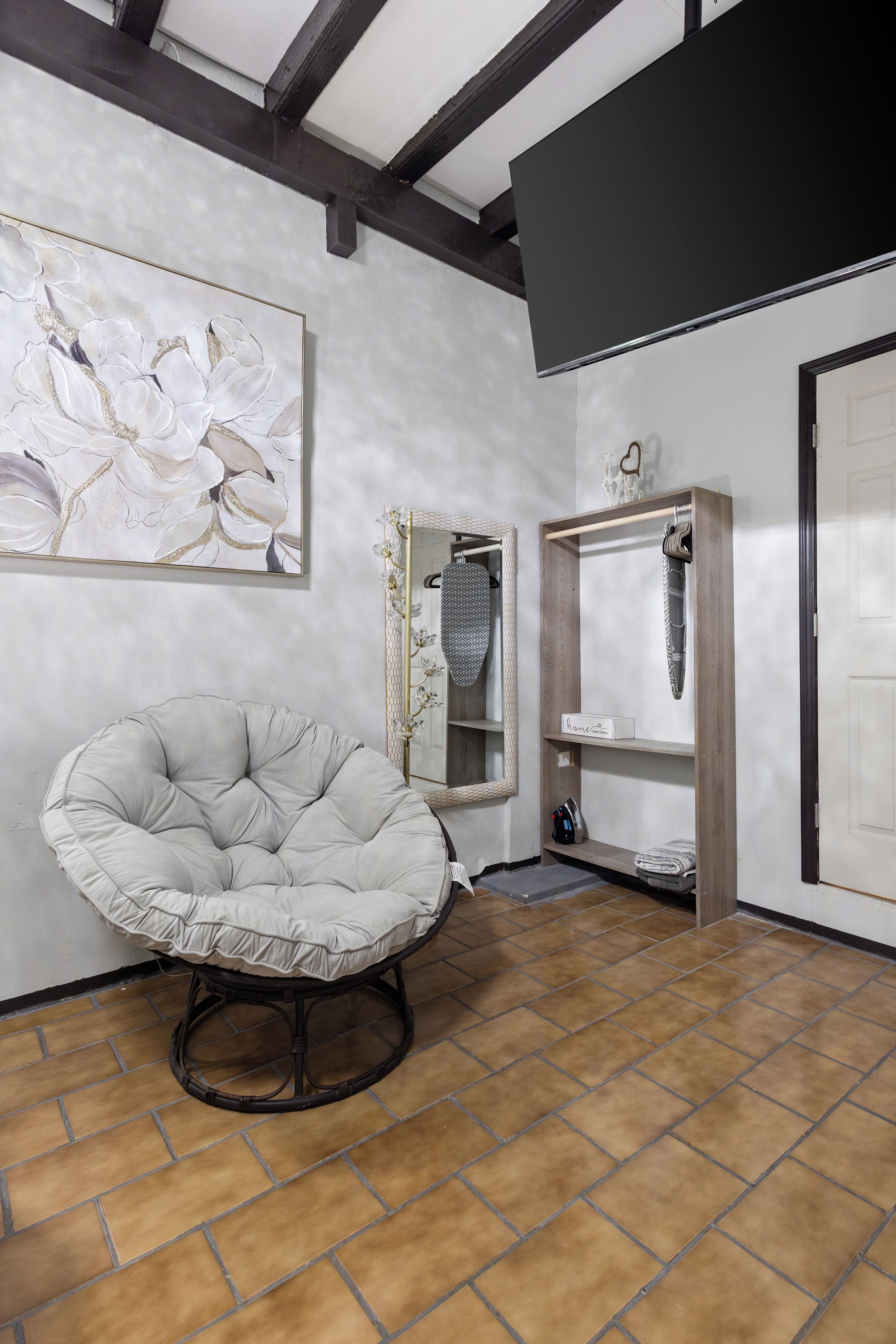 A room with a tufted chair, a large framed artwork, a decorative mirror, and a wooden shelf unit.