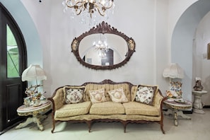 A room with a sofa, two side tables with lamps, a large ornate mirror, and a chandelier. - Casa Of Essence (San Juan)