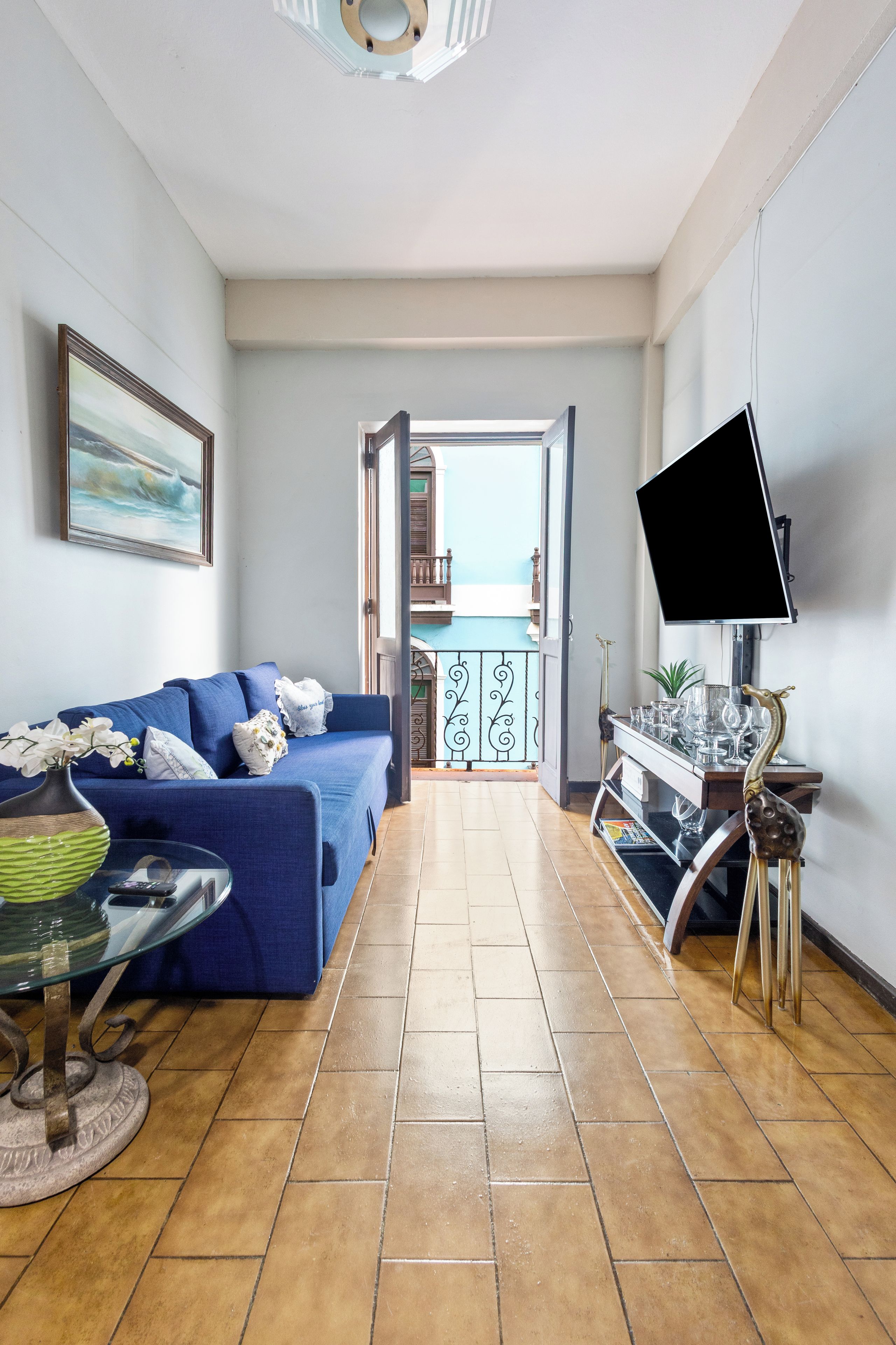Una sala de estar con un sofá azul, televisor y un balcón con vistas.