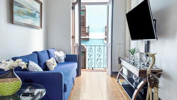 Una sala de estar con un sofá azul, televisor y un balcón con vistas.