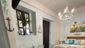 A bedroom with a blue marble floor, a bed with a headboard, a desk with a chair, a small table with a plant, and a chandelier. - Casa Of Essence (San Juan)