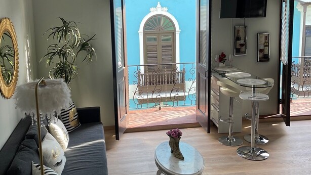 A modern living room with a sofa, a coffee table, and a balcony with a view of a building. - Casa Of Essence (San Juan)