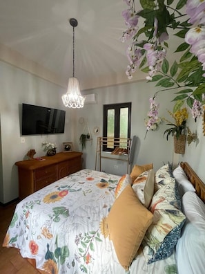 A bedroom with a large bed, a wooden dresser, a TV mounted on the wall, and a hanging light fixture. - Casa Of Essence (San Juan)
