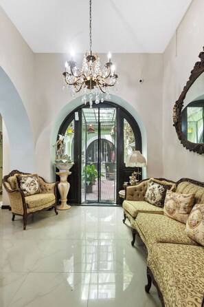 A spacious living room with a chandelier, two sofas, a coffee table, and a large arched doorway leading to an outdoor area. - Casa Of Essence (San Juan)