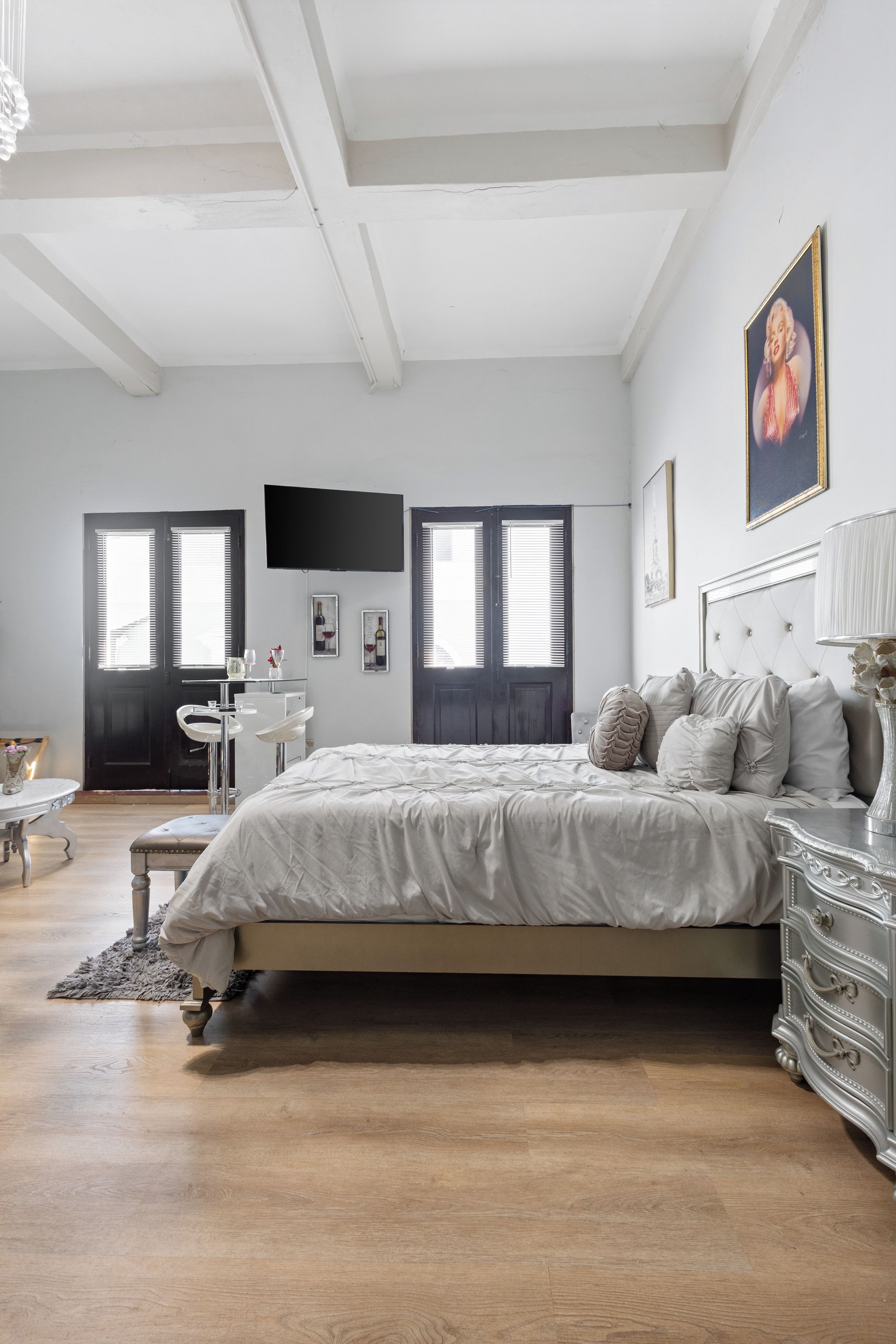 A bedroom with a large bed, a dresser, a vanity, and a television on the wall.