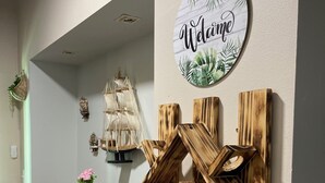A hallway with a wooden wall decor, a 'Welcome' sign, and various decorative items including a ship model, a rooster figurine, and a vase with flowers. - Casa Of Essence (San Juan)