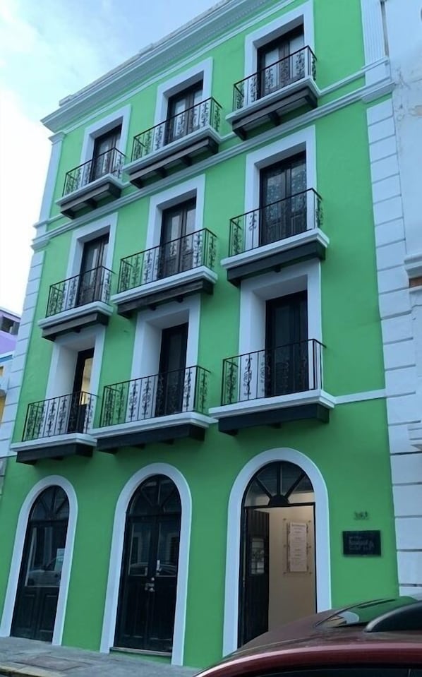 A multi-story building with green and white exterior walls, multiple balconies with black railings, and arched windows. - Casa Of Essence (San Juan)