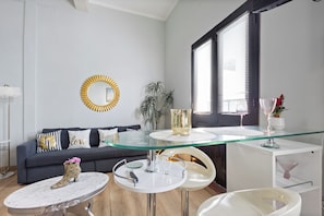 A modern living room with a glass-top coffee table, a grey sofa with decorative pillows, a round mirror, and a potted plant. - Casa Of Essence (San Juan)