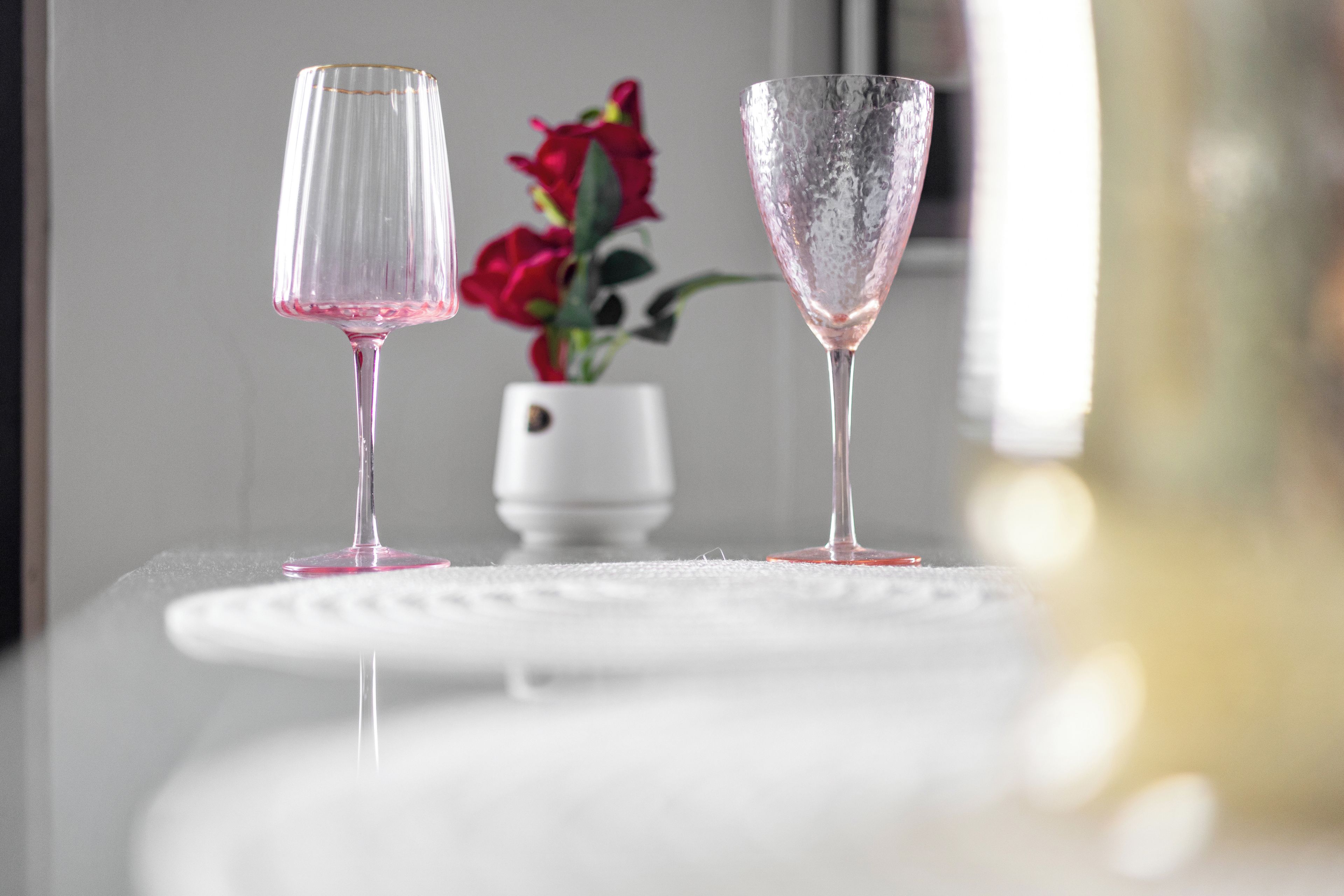 Two clear glass glasses on a white surface with a blurred background.