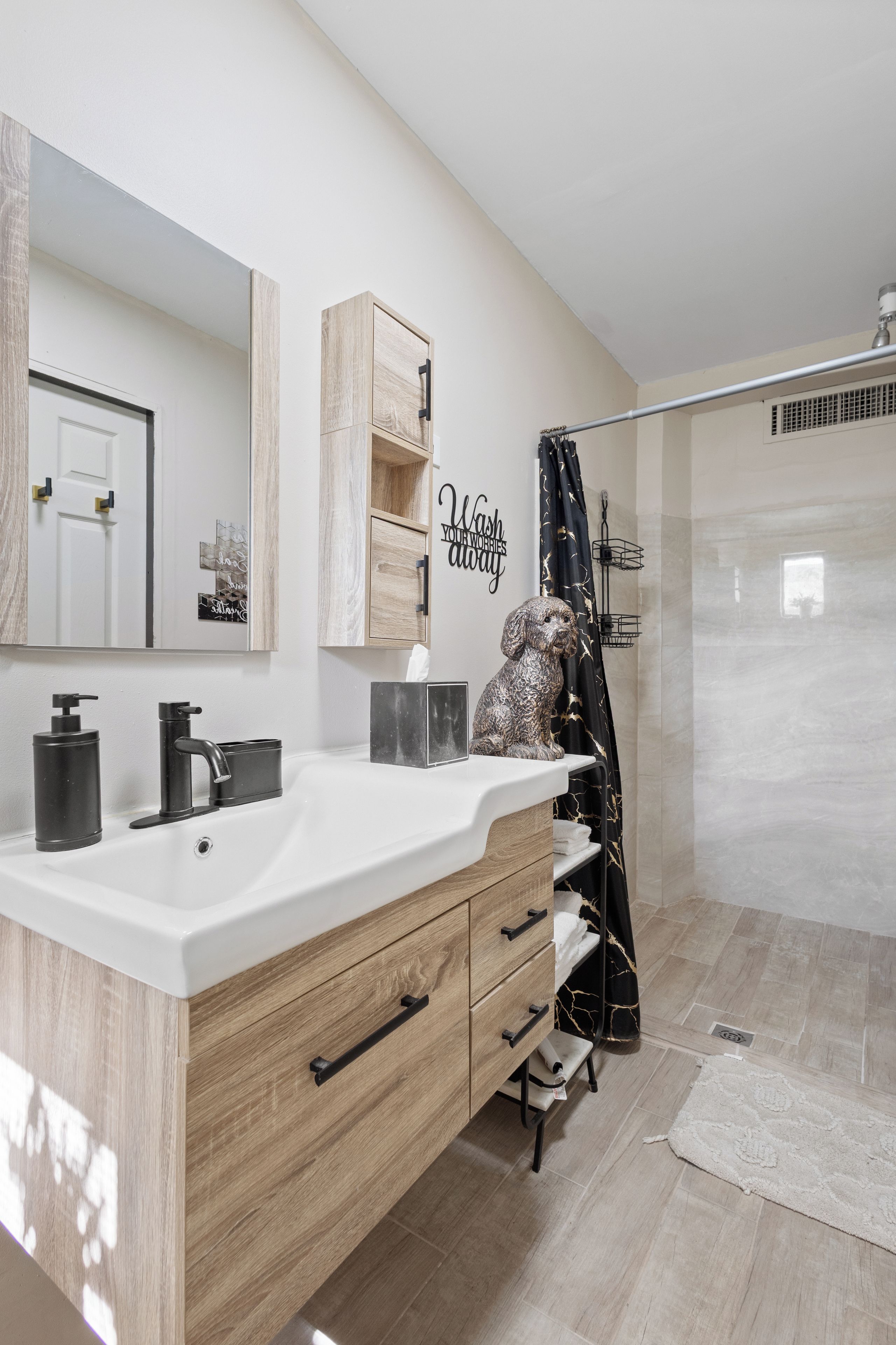 A modern bathroom with a large mirror, wooden vanity, black fixtures, and a shower area.