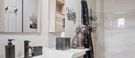 A modern bathroom with a large mirror, wooden vanity, black fixtures, and a shower area.