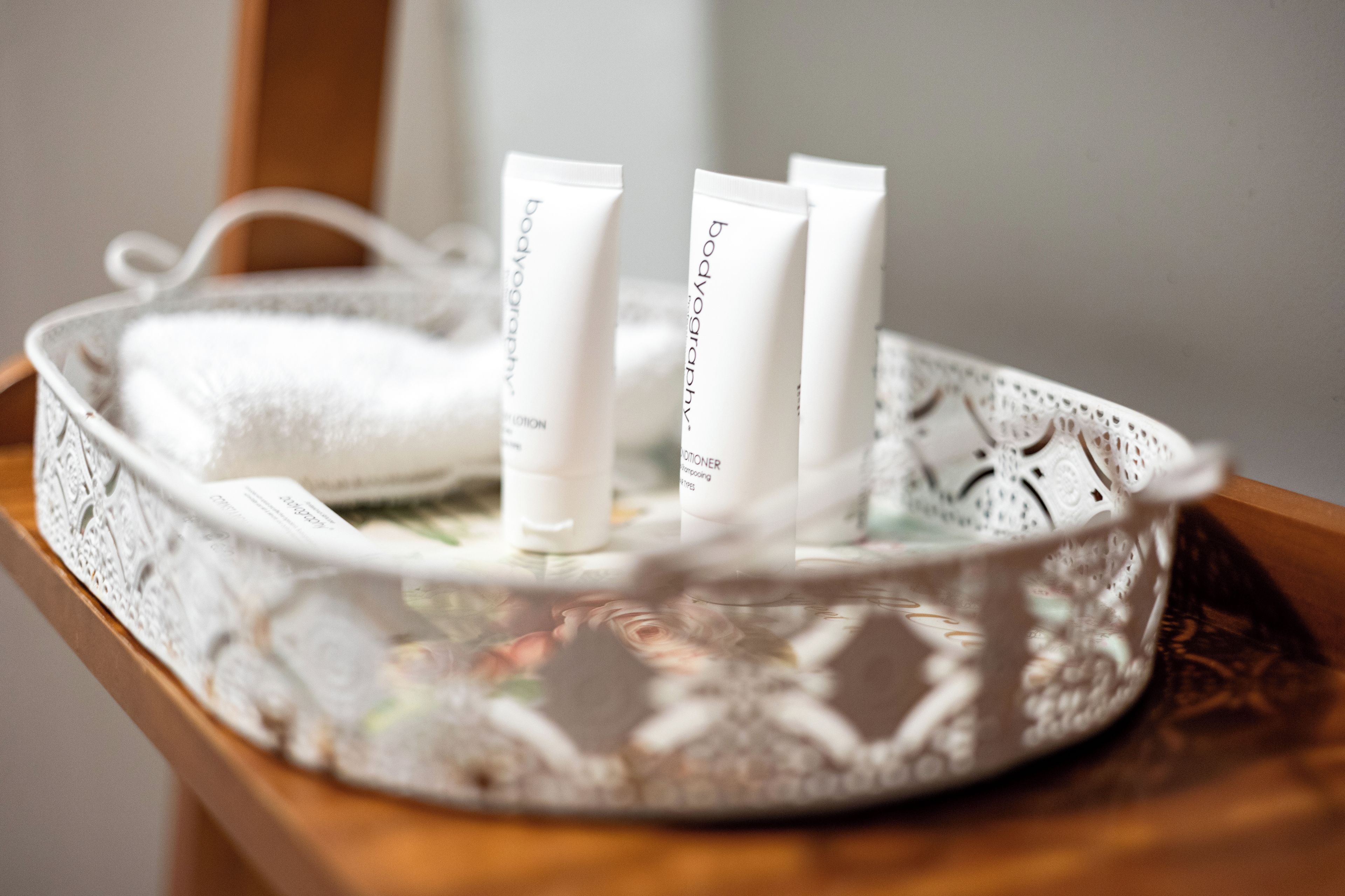 A tray with three tubes of body lotion and a white towel on a wooden surface.