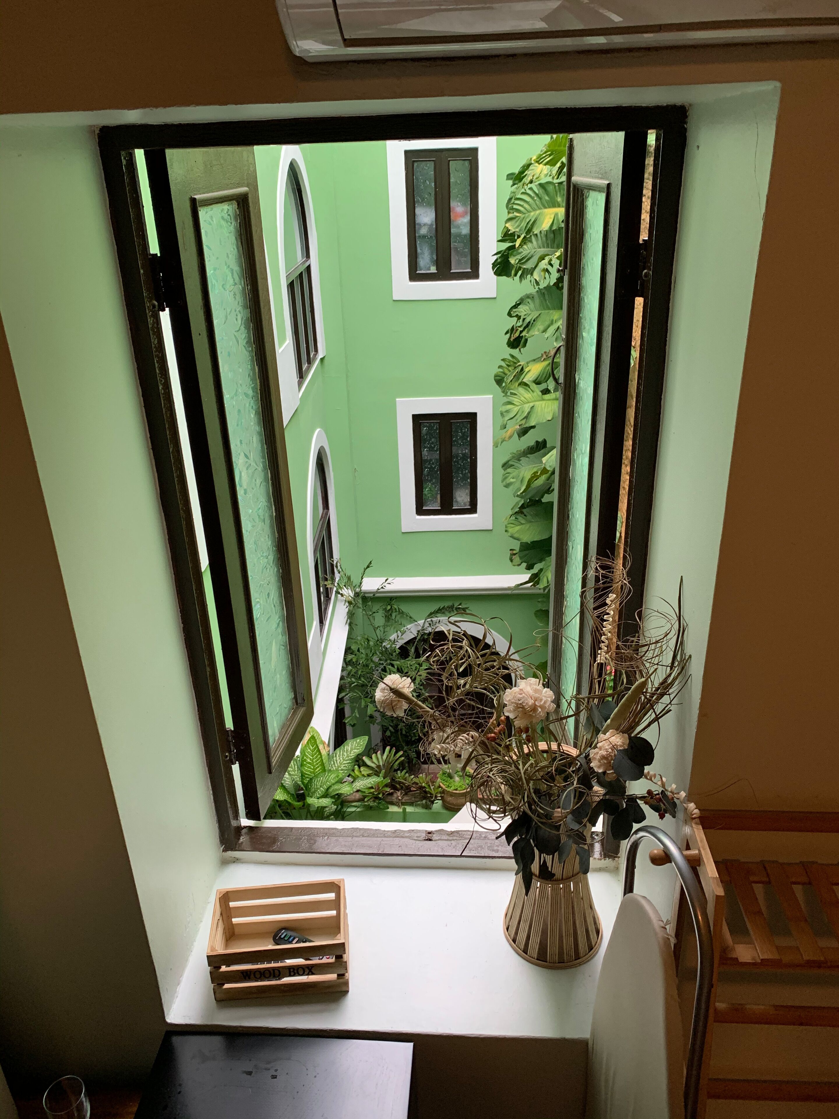 A window with a view of a green building, a wooden crate labeled "WOOD BOX," and a vase with flowers.