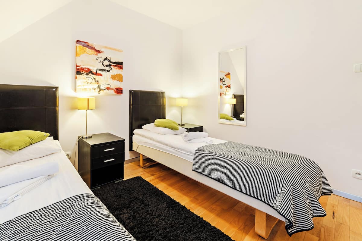 A hotel room with two single beds, a black leather headboard, a small bedside table with a lamp, and a mirror on the wall.